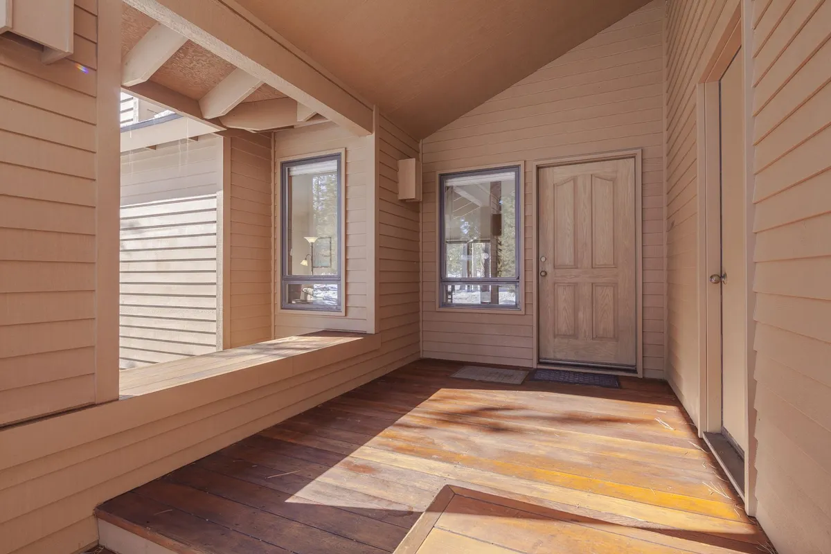 This image features the home's front door, large windows letting in plenty of natural light, and warm wooden flooring. The entryway suggests a welcoming transition between the outdoors and the interior, with a bench inviting guests to sit and relax.