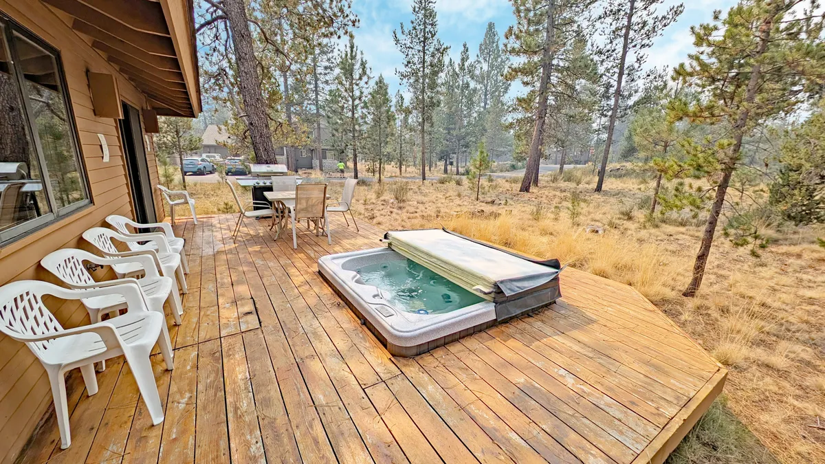 This image highlights the deck's inviting hot tub surrounded by wooden decking and comfortable outdoor chairs, all nestled among Sunriver’s iconic Ponderosa pines. The scene suggests a relaxing soak with views of the serene, forested landscape.
