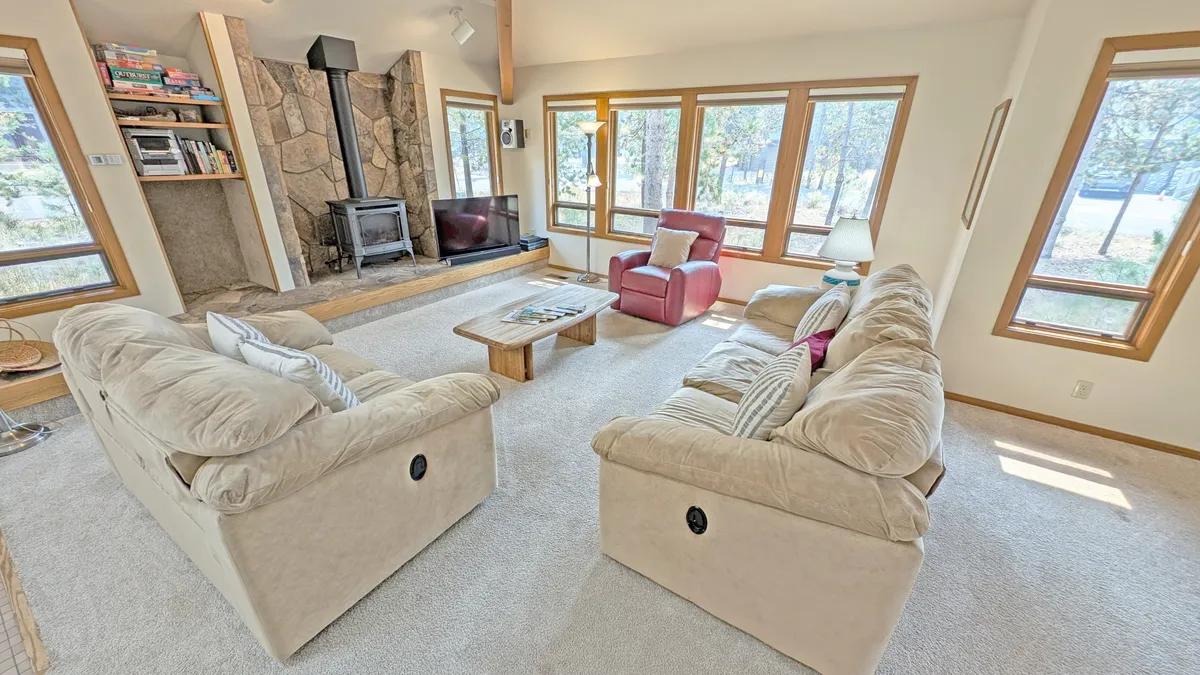 A warm, welcoming living room with a striking stone fireplace, large windows letting in natural light, and plush sofas. The room exudes comfort, ideal for cozying up with family or friends after an active day.