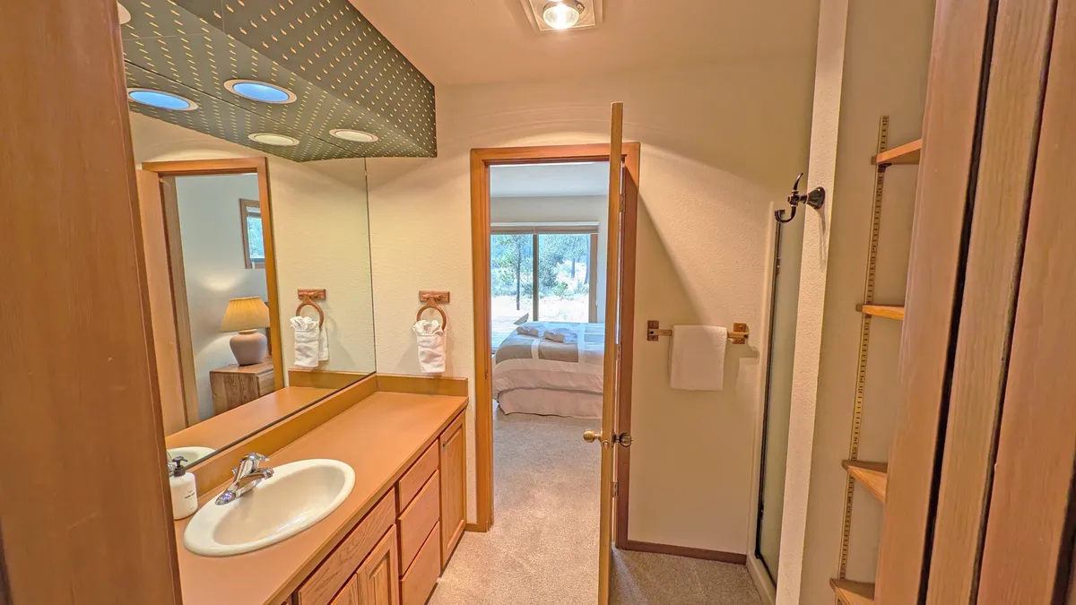 A serene bathroom featuring a vanity with sink, mirror, and doorway leading to a bedroom. Light fixtures provide a calm ambiance, and the layout suggests easy access and privacy—perfect for a relaxing bath or getting ready for bed.