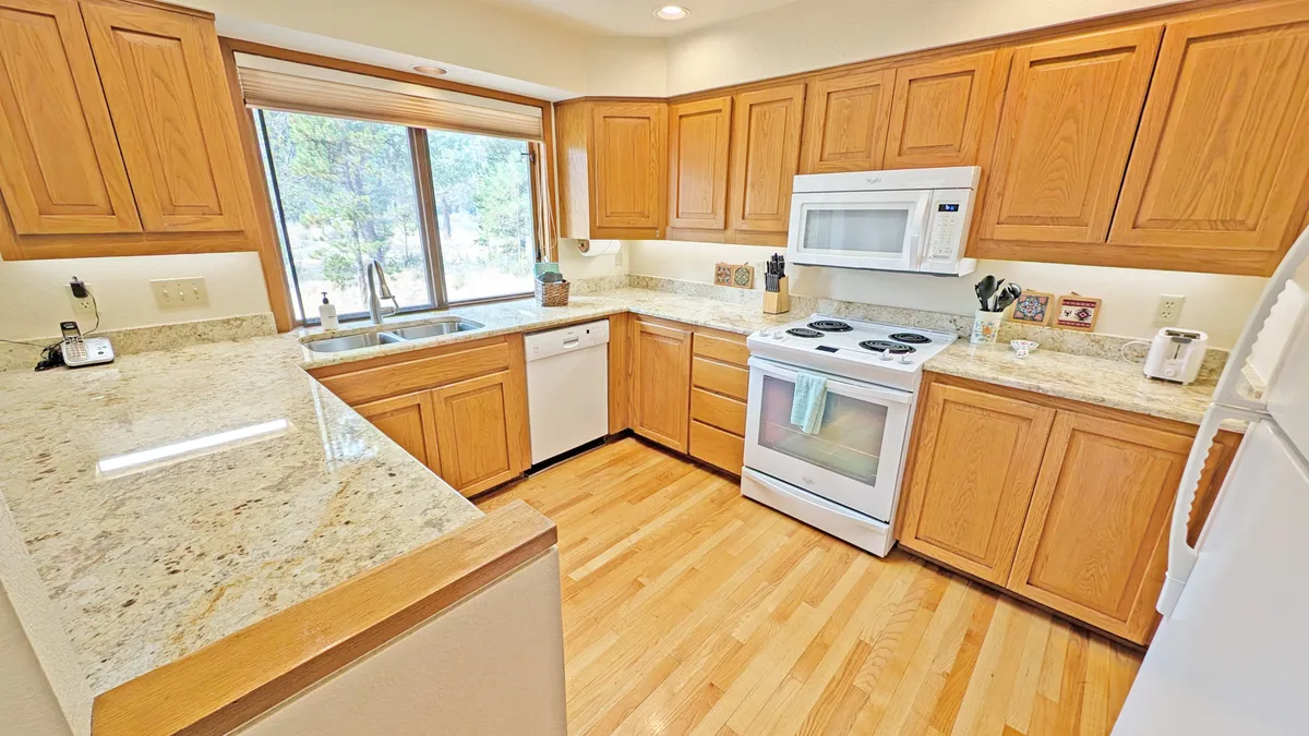 A modern, updated kitchen with granite countertops, wooden cabinets, stainless appliances, and a window letting in natural light. The space is set up for cooking and gathering, with enough room for multiple people to interact.