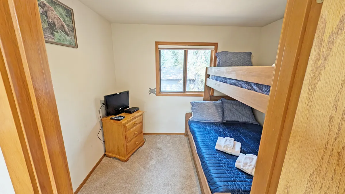A welcoming bedroom featuring a bunk bed, dresser, TV, and wall art. The window lets in natural light, making the room inviting for both kids and extra guests. The decor is playful yet functional, fostering a cozy and versatile environment.